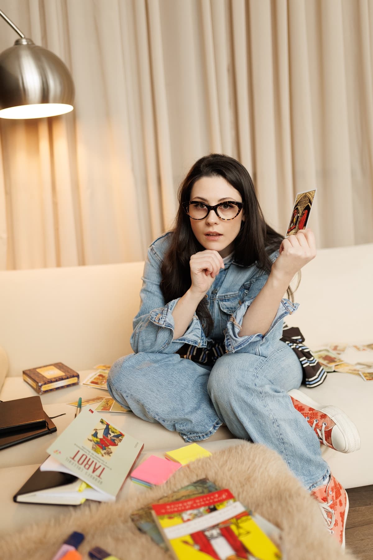 Ecaterina Axinia pe canapea, ridicând o carte de Tarot, cu cărți și o etalare în jur
