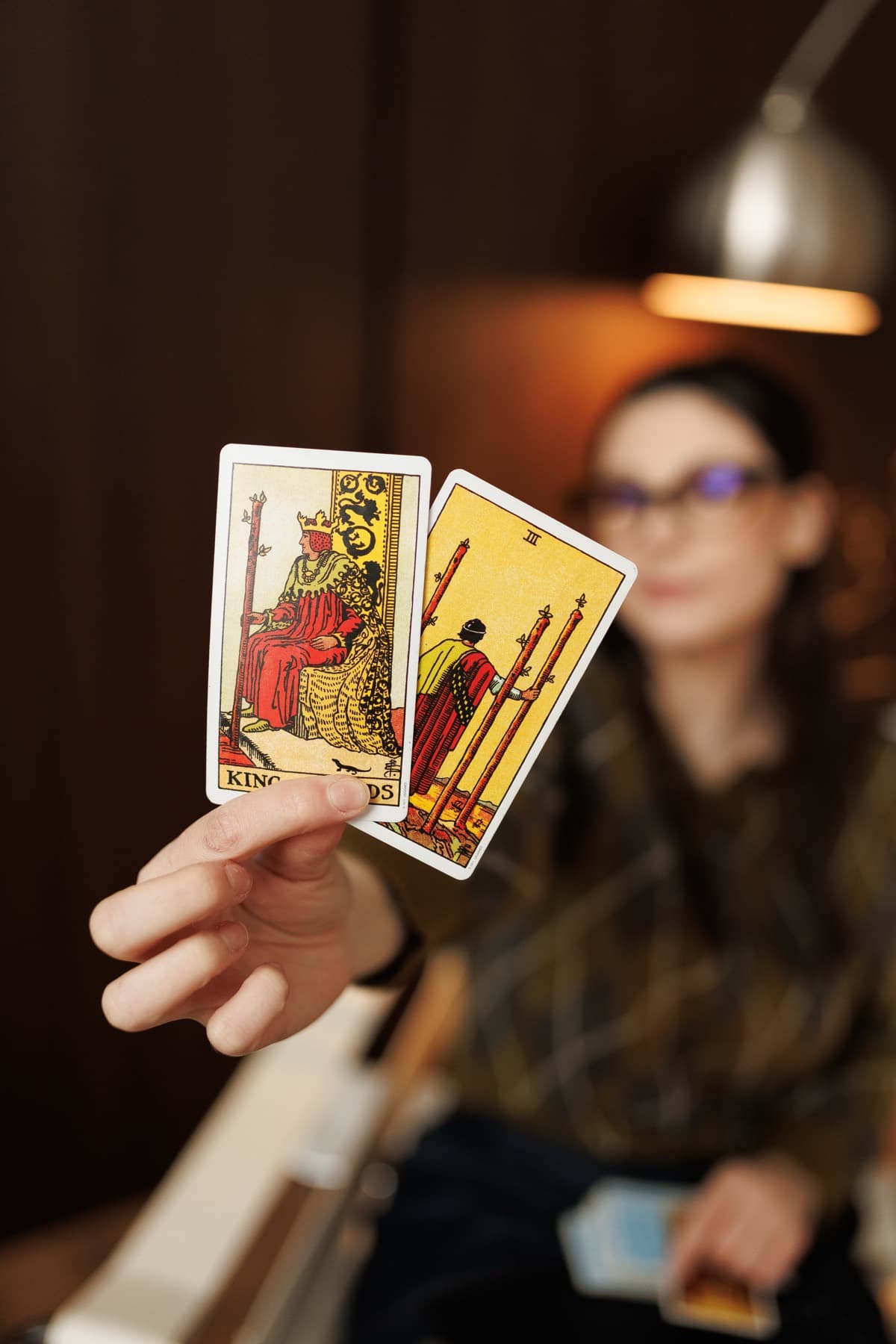Cursantă ținând în față două cărți de Tarot: Regele de Bâte și Trei de Bâte